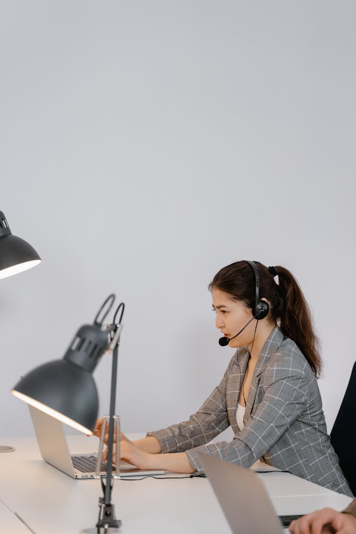 Photo of a Woman with a Black Headset Typing on Her Laptop